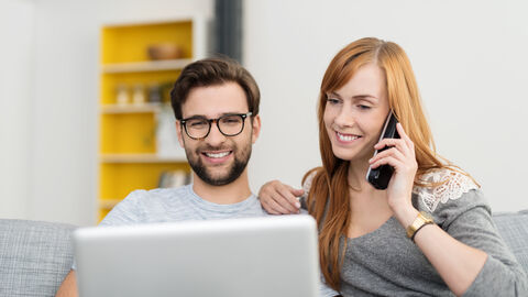 Glückliches Paar (Mann und Frau) mit Notebook und Telefon zu Hause auf der Couch.