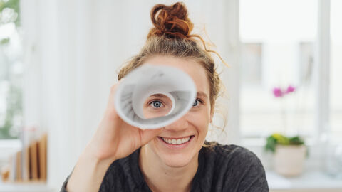 Finanzamt suchen! Junge Frau blickt durch Papierrolle wie mit einem Fernrohr.
