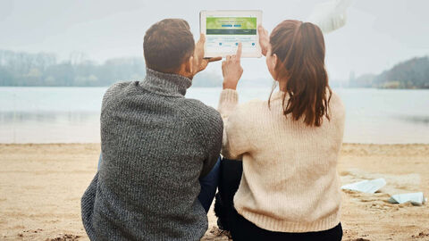 Frischer Wind für Ihre Steuererklärung! Junges Paar am Strand sieht sich ELSTER auf Tablet an