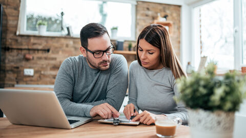 Steuererklärung 2021 elektronisch erstellen Frau und Mann sitzen konzentriert nebeneinander am Tisch vor einem Notebook und einem Klemmbrett.
