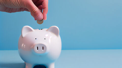 Hand wirft eine Münze in ein Sparschwein.